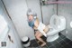 A woman with blue hair is sitting on a toilet.