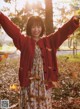 A young girl in a red cardigan standing in the leaves.