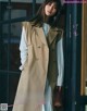 A woman wearing a trench coat standing in front of a window.