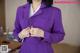 A woman in a purple suit is adjusting her tie.