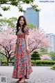 A woman standing in front of a tree wearing a floral dress.