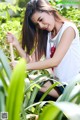 A woman in a white shirt and blue shorts crouching down in the grass.