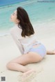 A woman in a white shirt and blue panties sitting on the beach.