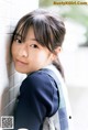 A young girl leaning against a wall with her hand on her chin.