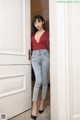 A woman in a red top and jeans standing in front of a door.