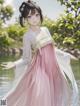 A woman in a pink and white dress standing by a lake.