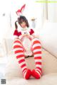 A woman in a red and white striped outfit sitting on a bed.