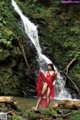 A woman in a red dress standing in front of a waterfall.