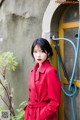 A woman in a red coat leaning against a wall.