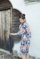 A woman in a blue and red floral kimono standing in front of a door.