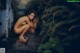 A naked woman sitting on a stone path in the woods.