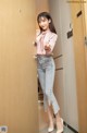 A woman in a pink shirt and jeans standing in front of a door.