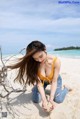 A woman in a yellow top and blue jeans on a beach.