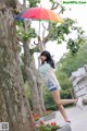 A woman standing next to a tree holding an umbrella.