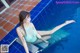 A woman in a blue bikini sitting on the edge of a swimming pool.