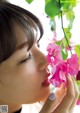 A woman smelling a pink flower in front of a window.