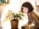 A woman sitting at a table next to a potted plant.